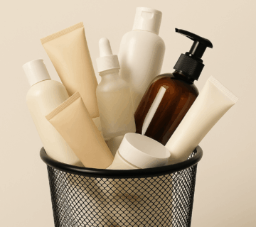 A variety of skin care products discarded in a mesh garbage bin.